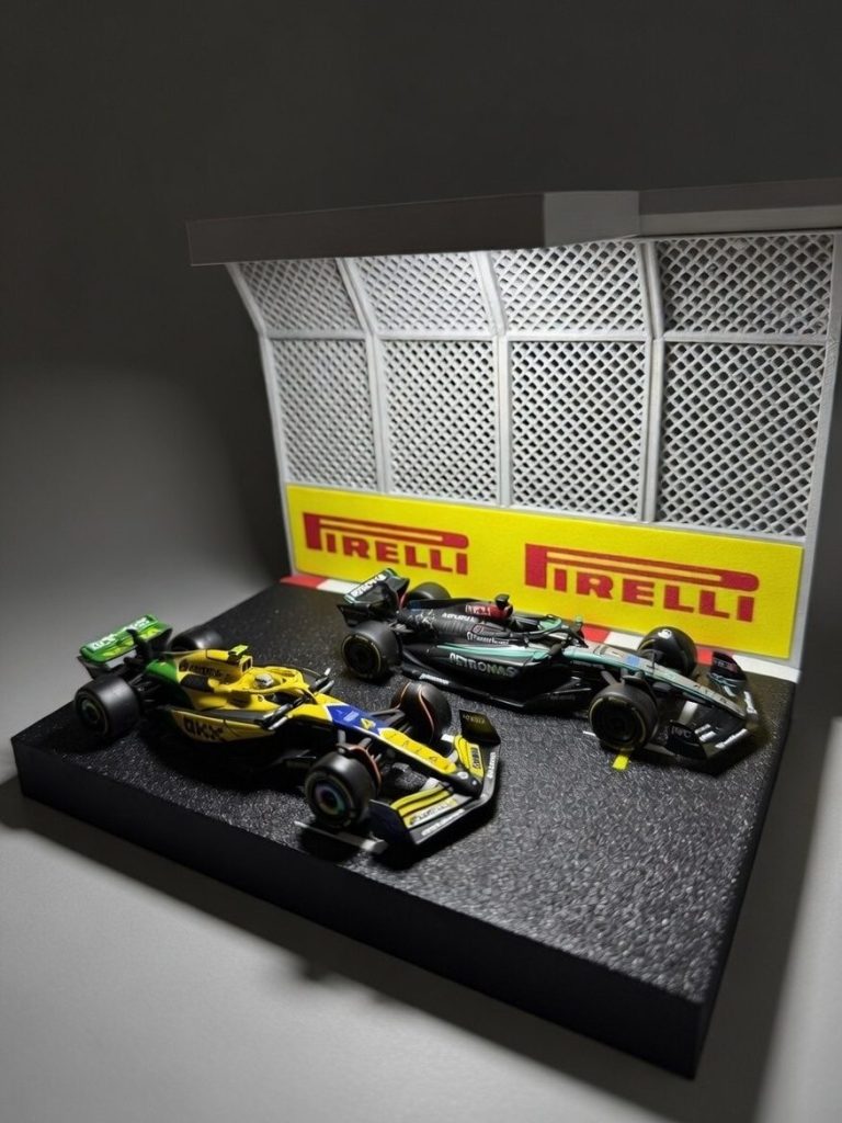 Drei Formel-1-Modellautos stehen vor einer Pirelli-Wand mit Gitterstruktur.